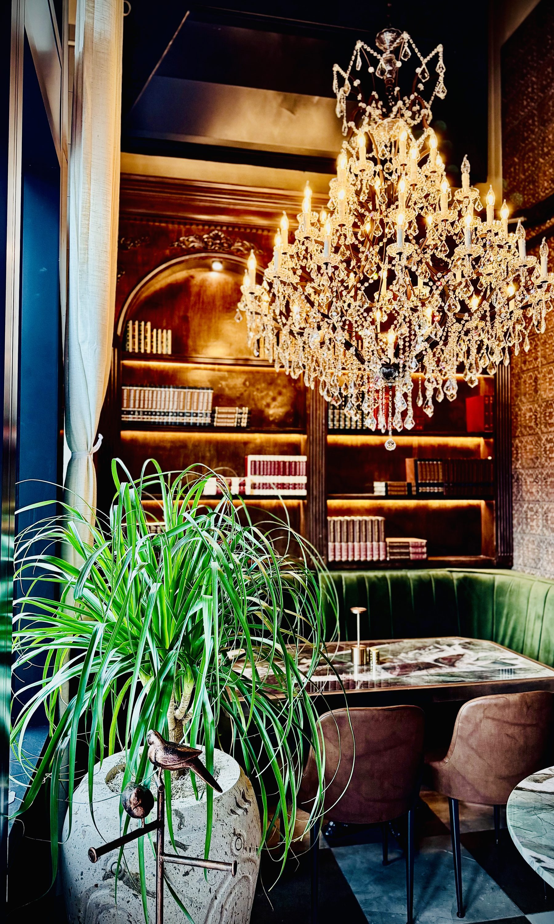 Restaurant install — grand chandelier over green velvet banquette